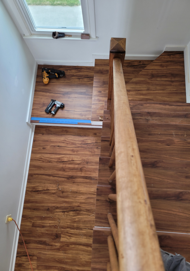 Wooden staircase with handrail under installation in residential foyer.