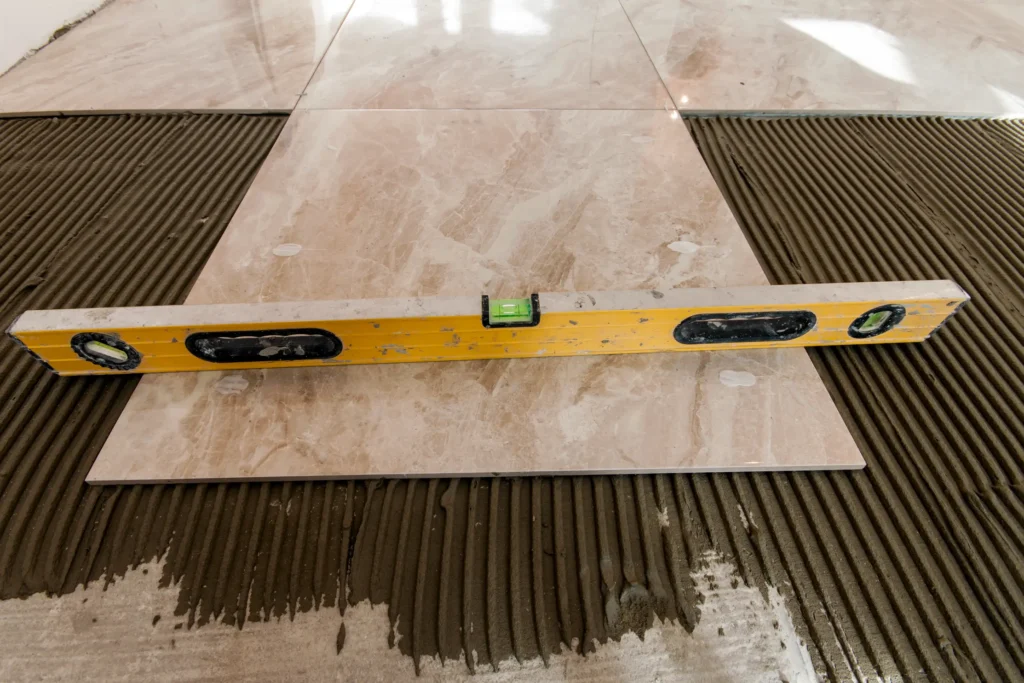 A level tool resting on a tile placed on a subfloor, demonstrating the process of checking for levelness before installing new flooring. The image emphasizes the importance of subfloor leveling for a successful flooring installation.
