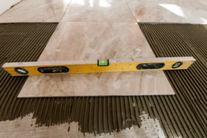 A level tool resting on a tile placed on a subfloor, demonstrating the process of checking for levelness before installing new flooring. The image emphasizes the importance of subfloor leveling for a successful flooring installation.