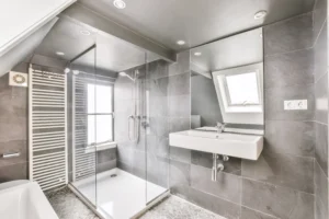 A modern bathroom showcasing a stylish shower area with contemporary gray tiles. The bathroom features a clean, minimalist design with a frameless glass shower enclosure and a sleek sink.