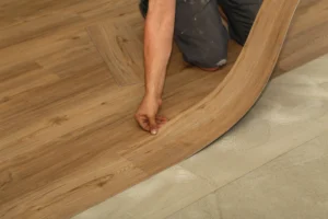 A person's hand carefully placing a luxury vinyl plank during installation, showcasing the precise and detailed nature of the process. The image highlights the modern and stylish appearance of the flooring.